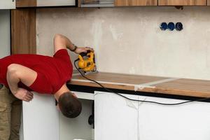 vakman, meubilair maker en assembler, installeert een modern keuken in de huis met gereedschap in hand. Op maat meubilair concept, huis verbetering, vernieuwing foto