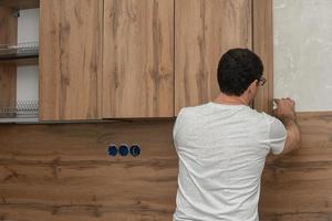 vakman, meubilair maker en assembler, installeert een modern keuken in de huis met gereedschap in hand. Op maat meubilair concept, huis verbetering, vernieuwing foto