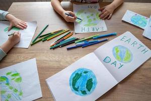kinderen trek de planeet aarde met potloden en viltstift pennen Aan album lakens voor aarde dag Bij hun huis tafel. foto
