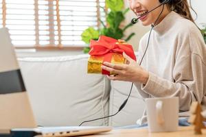 vieren Aan dag van liefde, nieuw jaar seizoen, Aziatisch gelukkig mooi jong vrouw vervelend koptelefoon, koptelefoon en groet Aan video telefoontje gedurende sociaal afstand, hand- in tonen Cadeau, geschenk doos Aan valentijn. foto