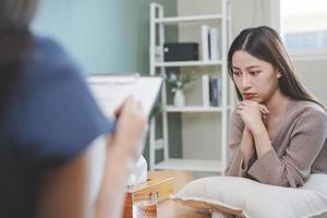 psychologie, depressie. verdrietig, lijden Aziatisch jong vrouw overleg plegen met psycholoog, psychiater terwijl geduldig begeleiding mentaal met dokter vrouw nemen aantekeningen Bij kliniek. bemoedigend, therapie. foto