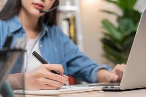 video telefoongesprek, vergadering conferentie via camera, gelukkig mooi Aziatisch jong vrouw, meisje zitten, slijtage draadloze koptelefoon studie online, gebruik makend van laptop computer, freelancer werkende.technologie, sociaal afstand. foto