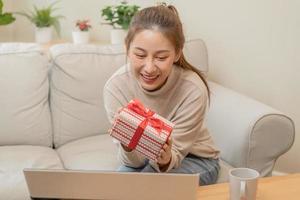 vieren Aan dag van liefde, nieuw jaar dag seizoen, mooi Aziatisch jong vrouw, meisje gebruik makend van laptop computer, groet Aan video telefoontje gedurende sociaal afstand, Holding geschenk doos, gelukkig naar krijgen Cadeau Aan valentijn. foto