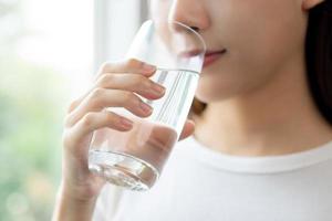 gelukkig mooi, Aziatisch jong vrouw, meisje drinken, slokje vers glas van water voor hydratatie van lichaam, Holding transparant glas in haar hand, dorstig Bij huis. Gezondheid zorg, gezond levensstijl concept. foto