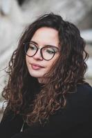 mooi jong vrouw met brunette gekruld haar, portret in oog bril genieten van de zon in de stad. foto