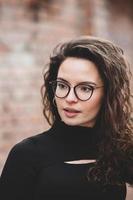 mooi jong vrouw met brunette gekruld haar, portret in oog bril genieten van de zon in de stad. foto