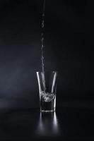 een stroom van alcohol giet in een glas tegen een zwart achtergrond. water plons. dichtbij omhoog foto