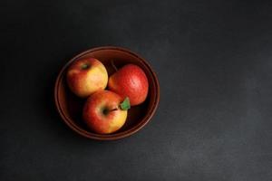 drie rood sappig appels liggen in een klei bord tegen een zwart achtergrond. kopiëren ruimte foto