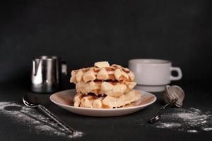 eigengemaakt van smakelijk belgisch wafels bord, karamel saus, koffie beker, melk Aan een zwart beton achtergrond foto