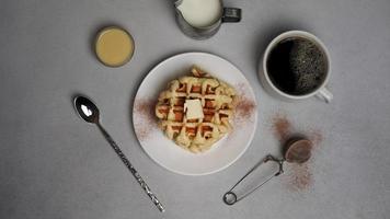 top visie van smakelijk wafels bord, karamel saus, koffie beker, melk, dessert lepel, zeef Aan een grijs beton achtergrond foto