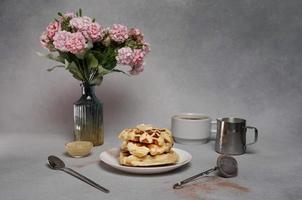 eigengemaakt van smakelijk wafels bord, karamel saus, koffie beker, melk, roze bloemen Aan een grijs achtergrond foto