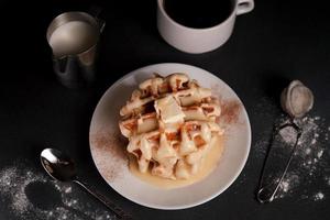 eigengemaakt van smakelijk belgisch wafels bord, karamel saus, koffie beker, melk Aan een zwart beton achtergrond foto