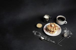 eigengemaakt van ontbijt smakelijk wafels, karamel saus, koffie beker, melk, dessert lepel, zeef Aan een zwart beton achtergrond foto