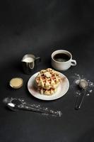 eigengemaakt van ontbijt smakelijk wafels, karamel saus, koffie beker, melk, dessert lepel, zeef Aan een zwart beton achtergrond foto