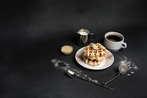 eigengemaakt van ontbijt smakelijk wafels, karamel saus, koffie beker, melk, dessert lepel, zeef Aan een zwart beton achtergrond foto