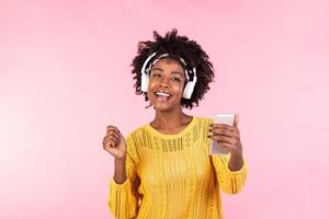 levensstijl concept - portret van mooi Afrikaanse Amerikaans vrouw blij luisteren naar muziek- Aan mobiel telefoon. modieus elegant schattig meisje in hoofdtelefoons luisteren naar muziek- dansen geïsoleerd roze achtergrond foto