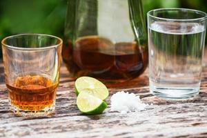 alcoholisch drankjes en citroen zout Aan rustiek hout achtergrond brandewijn in een glas met alcohol flessen en water wodka rum cognac tequila en whisky concept foto