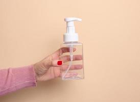 vrouw hand- houdt leeg plastic houder met dispenser voor vloeistof producten, zeep of shampoo Aan beige achtergrond foto