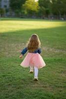 een weinig meisje 3 jaren oud in een zomer jurk loopt weg van de camera. de meisje is draaide zich om rug. zomer tijd. foto