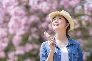 Aziatisch vrouw Holding de zoet Hanami dango toetje terwijl wandelen in de park Bij kers bloesem boom gedurende voorjaar sakura festival met kopiëren ruimte foto