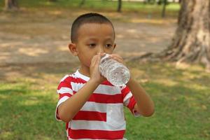 jongen spelen drinken water in de park foto