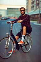 Mens in zonnebril rijden een fiets Aan stad straat foto