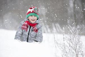 kind in winter voor een wandelen. een weinig jongen, in een rood gebreid hoed, zit in een sneeuwjacht. foto
