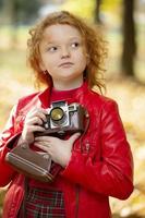 weinig roodharig meisje met een retro camera Aan een herfst achtergrond.weinig roodharig meisje met een retro camera Aan een herfst achtergrond. foto