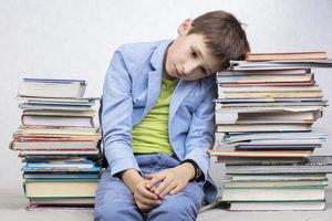 een moe school leeftijd jongen zit tussen stapels van boeken. verdrietig kind met boeken. foto