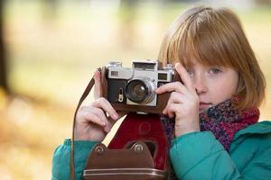 weinig roodharig meisje met een retro camera in de herfst park. kind fotograaf. foto