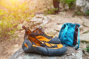 oranje beklimming schoenen en magnesium in een blauw zak staan Aan een steen. beklimming kleding foto