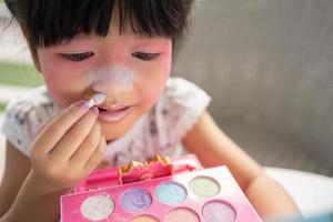 aanbiddelijk weinig kind Aziatisch meisje verven haar mond met roze kinderen hoofden en looks in de spiegel. een kind Toneelstukken Bij huis in een speelgoed- schoonheid salon. toenemen aan het leren ontwikkeling voor kleuters. foto