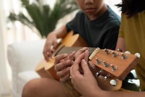 Aziatisch jongen spelen gitaar met mam in de leven kamer voor onderwijs hem zoon Speel gitaar, voelen gewaardeerd en aangemoedigd. concept van een gelukkig familie, aan het leren en pret levensstijl, liefde familie banden foto