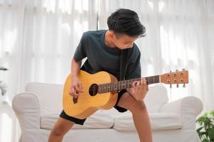 portret van een Aziatisch gelukkig glimlachen jongen hebben pret spelen gitaar muziek- concept, kinderen muziek- school. rots concert, muziek- voor kinderen en peuters concept foto