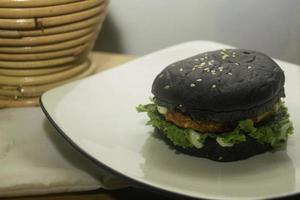 dichtbij omhoog foto van de geopend zwart hamburger Aan een wit bord is zeer geschikt voor een snel voedsel menu