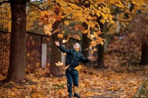 een jongen in de herfst Woud gooit bladeren en verheugt zich foto