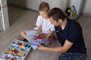 een schattig jongen in een wit t-shirt verzamelt een elektrisch ontwerper met zijn vader in de kamer foto