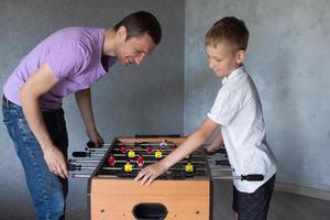 schattig jongen spelen tafel Amerikaans voetbal met zijn emotioneel vader in de kamer foto