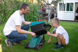 vader en zijn nieuwsgierig zoon maaien de gazon. demonteren de gazon maaier foto