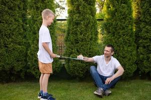 een vrolijk vader Aan de straat ondersteunt zijn zoon. een jongen is spelen badminton in een wit t-shirt foto