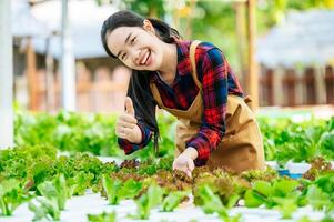 jong Aziatisch meisje boer tonen duim omhoog met vers groen eik sla salade, biologisch hydrocultuur groente in kinderkamer boerderij. bedrijf en biologisch hydrocultuur groente concept. foto