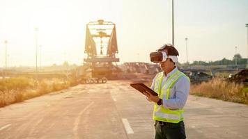 Aziatisch ingenieur gebruik makend van virtueel realiteit koptelefoon en tablet voor inspecteren en werken Bij bouw plaats foto