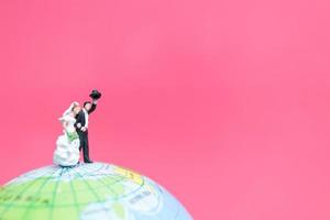 miniatuur bruid en bruidegom op een wereldbol met een roze achtergrond, Valentijnsdag concept foto