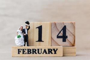 miniatuurpaar met houten blokken 14 februari-tekst op een houten achtergrond, het concept van de gelukkige Valentijnsdag foto