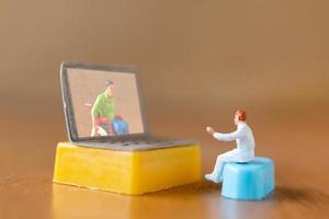 miniatuur mannelijke patiënt overleggen met een arts met behulp van een videogesprek op een laptop, online doktersconcept foto