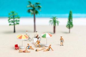 miniatuurmensen die zwemkleding dragen die op een strand met een blauwe achtergrond ontspannen foto