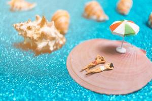 miniatuurmensen die zwemkleding dragen die op een zeeschelp ontspannen met een glitterachtergrond foto
