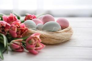 een nest met eieren in teder pastel kleuren en een boeket van tulpen Aan een wit achtergrond foto