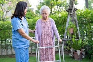 dokter verzorger helpen en zorg Aziatisch senior vrouw geduldig wandelen met wandelaar in park Bij ziekenhuis. foto