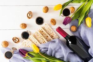 zilver bril met rood wijn, matza, een fles van wijn en tulpen Aan een wit houten achtergrond. de concept van de Joods Pascha vakantie. foto